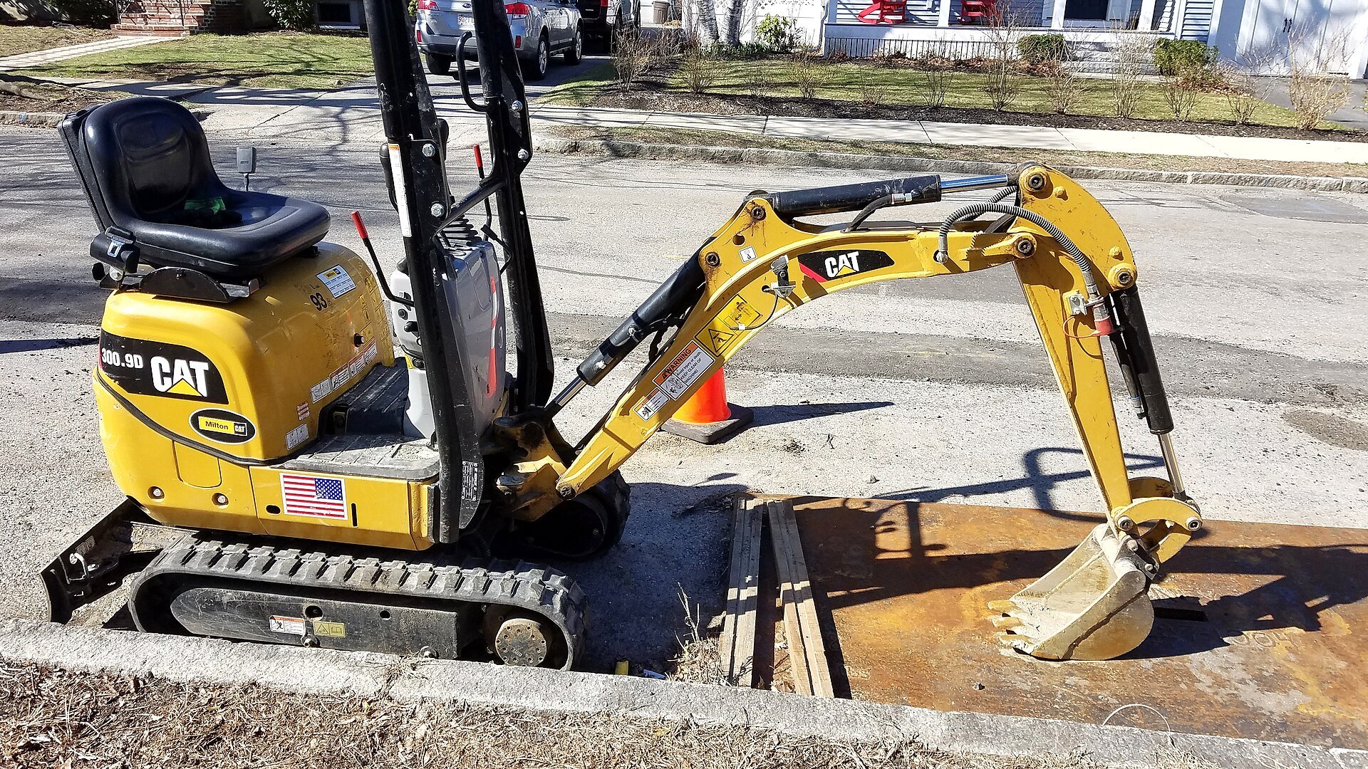 Caterpillar 300.9D mini excavator working a curb cut on a green residential street