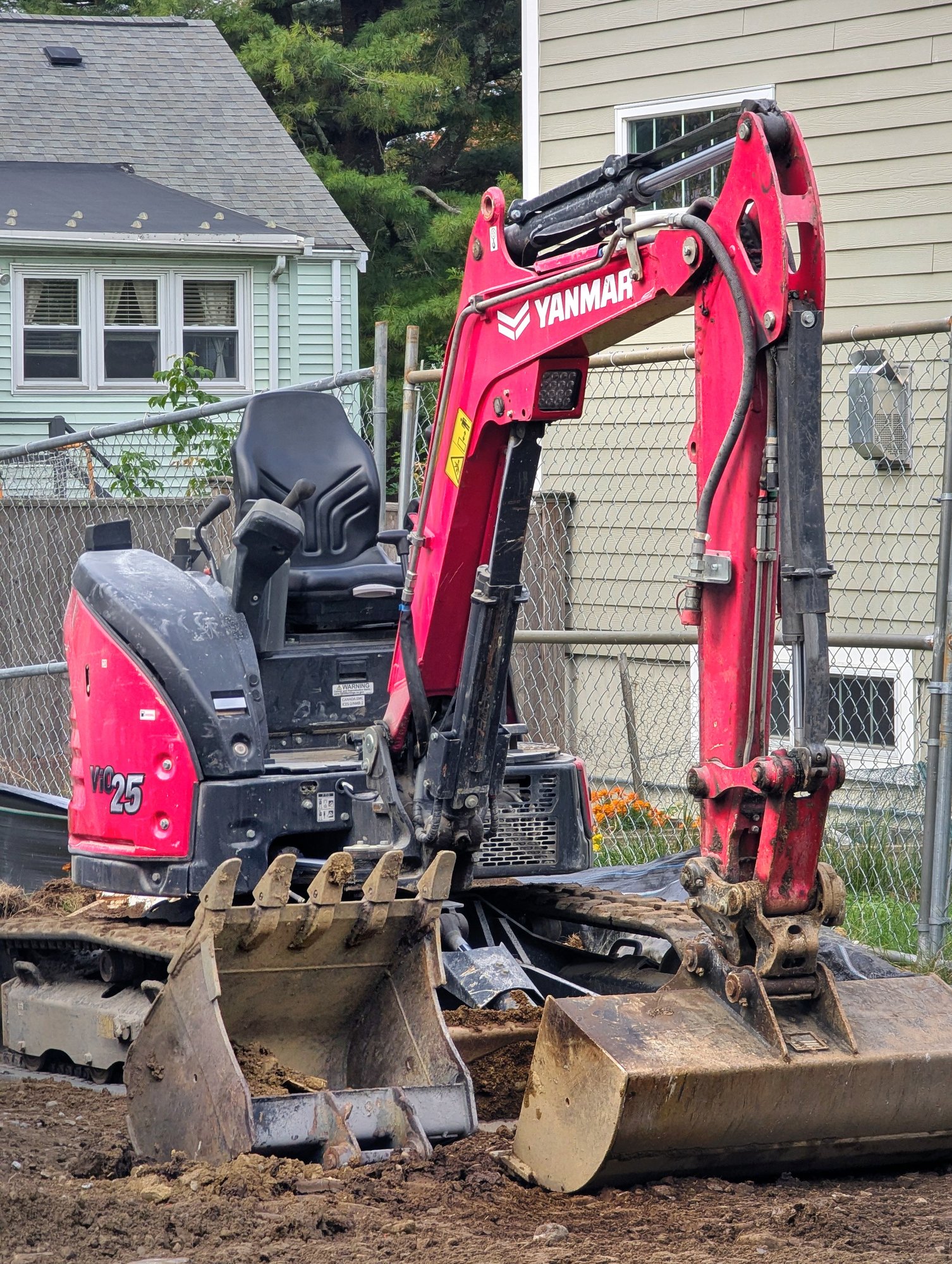 Yanmar ViO25 mini excavator on clay soil beside houses and a fence
