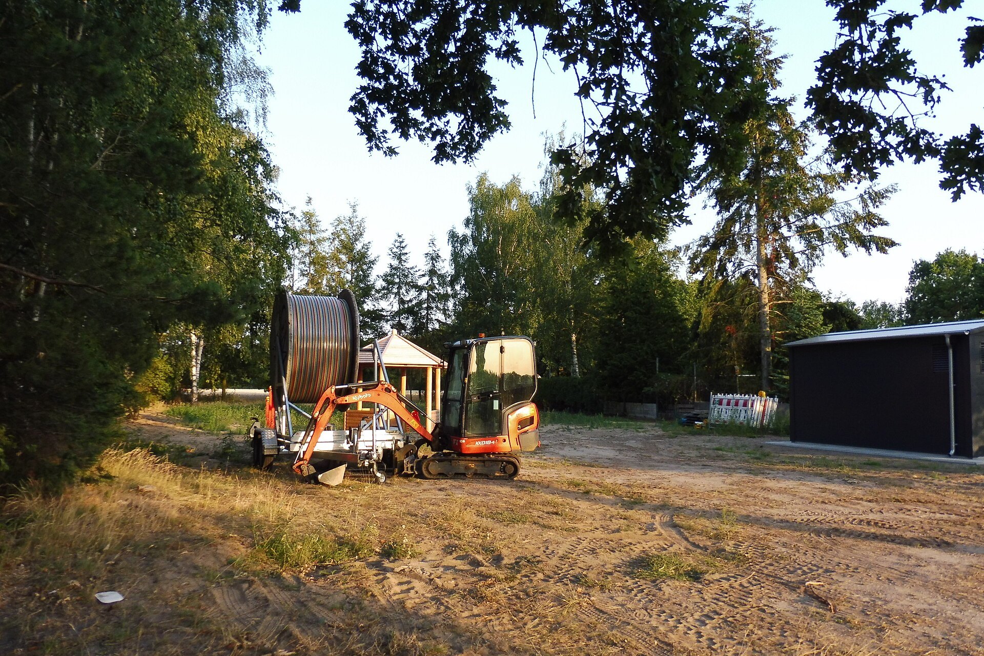 Kubota KX018-4 mini excavator beside a cable reel on a dirt work pad with trees
